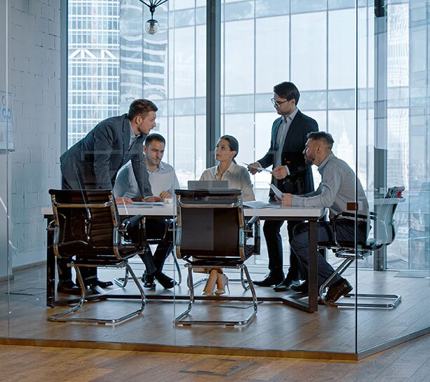 Diverse group of business professionals collaborating in a modern office, engaged in a meeting and discussing ideas near large glass windows in an urban setting.